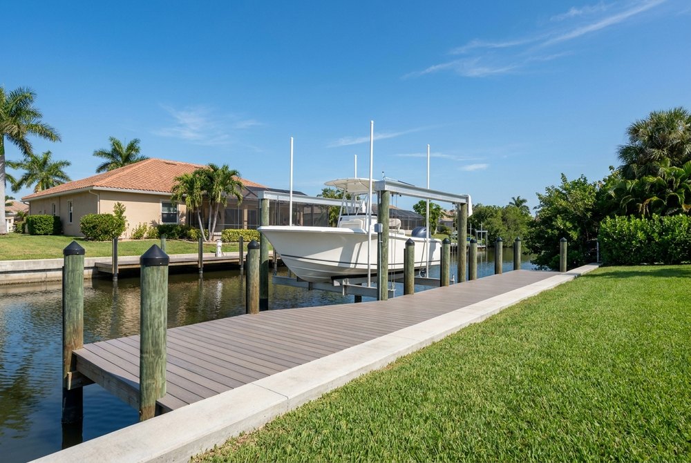 Composite dock deck beside a concrete seawall cap, a white center console raised on a four-post boat lift, with a tile-roof home and palms on a calm canal